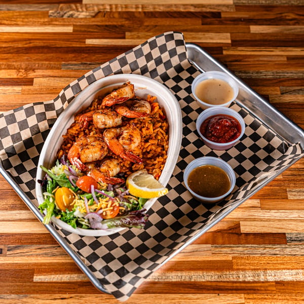 Shrimp and rice bowl with a side salad, lemon wedge, and three dipping sauces on a tray.
