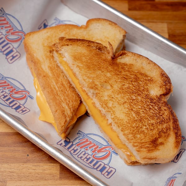 Golden-brown grilled cheese sandwich halves with melted yellow cheese on branded Clutch City Grill paper.