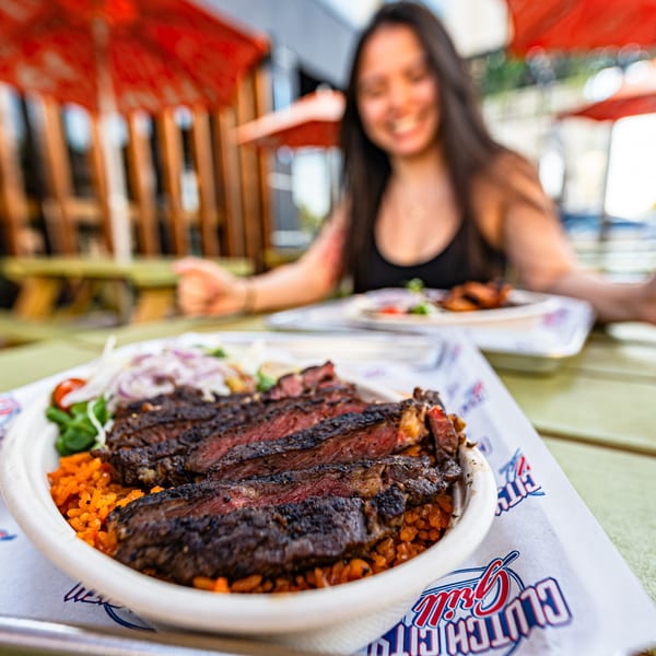 Clutch City Grill's sliced steak with rice and salad, with a smiling woman in the background.
