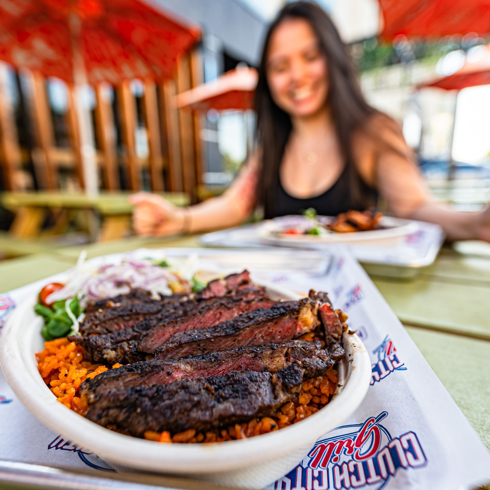 Clutch City Grill's sliced steak with rice and salad, with a smiling woman in the background.