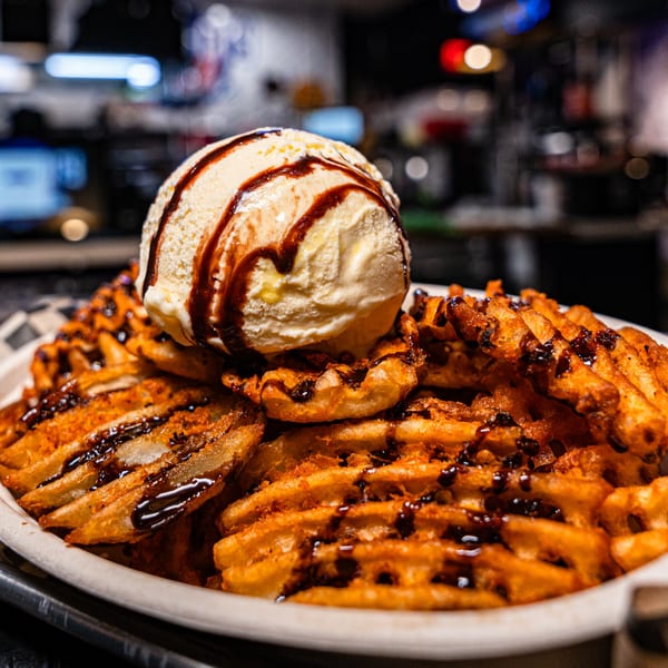 Waffle fries drizzled with chocolate sauce, topped with a scoop of vanilla ice cream.