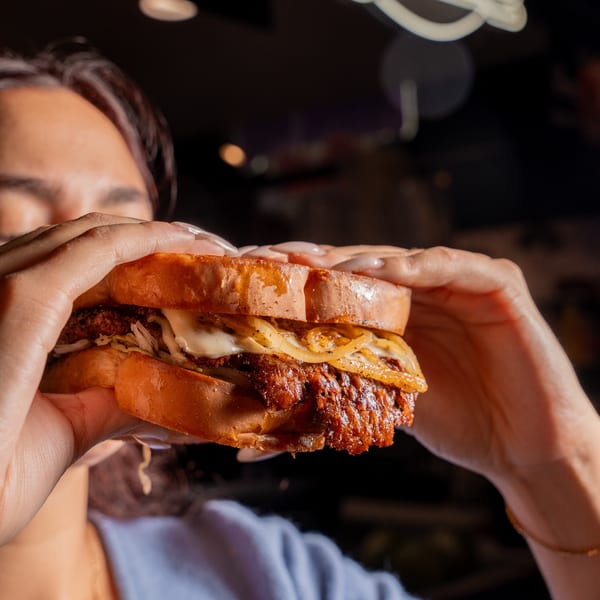 A person holds a large, juicy Clutch City Grill sandwich with melted cheese and caramelized onions.