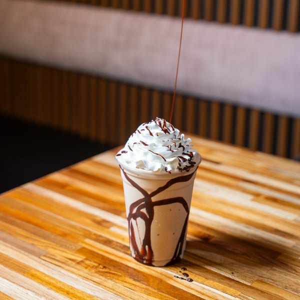 Chocolate milkshake with whipped cream and chocolate drizzle on a wooden table at Clutch City Grill.