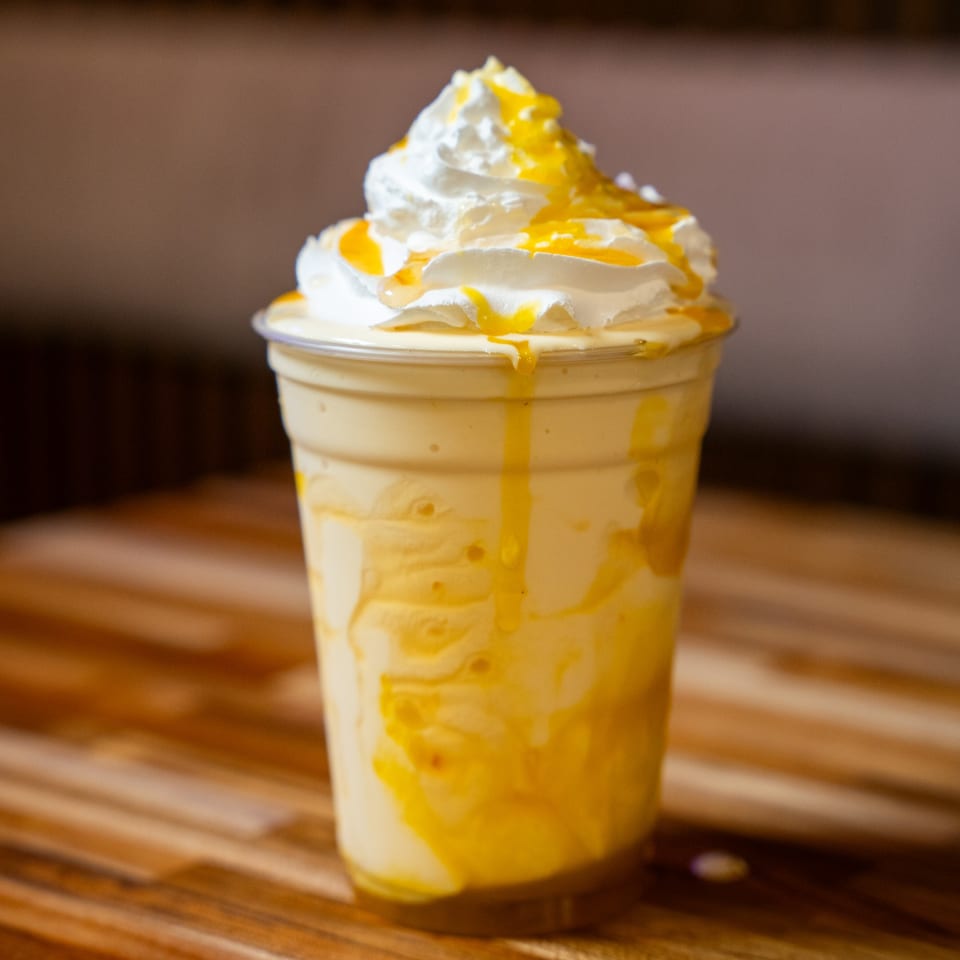 A creamy yellow milkshake with whipped cream and yellow syrup drizzle in a clear plastic cup.
