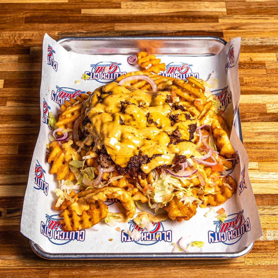 Loaded waffle fries from Clutch City Grill, topped with ground beef, cheese sauce, lettuce, and red onions.