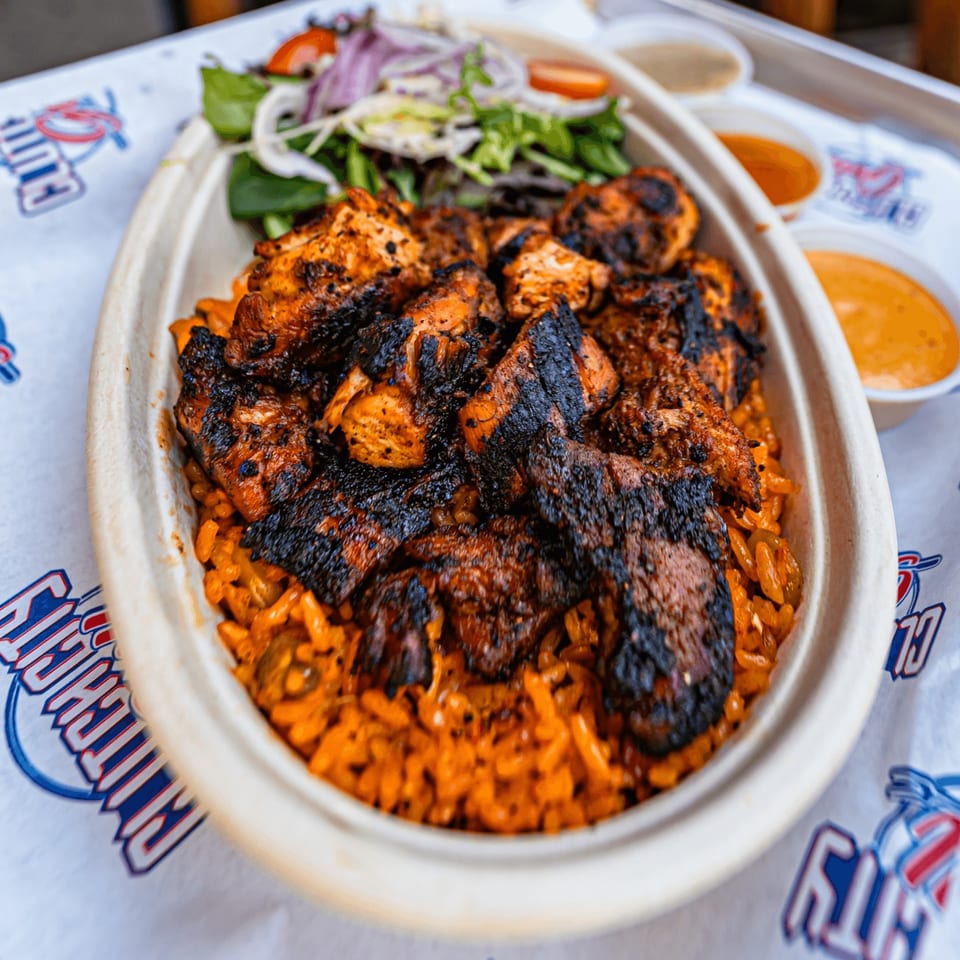 Grilled chicken pieces over orange rice with a side salad in a Clutch City Grill bowl.
