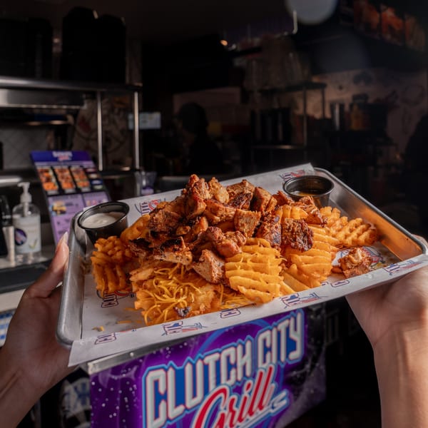 Hands holding a tray of waffle fries, shredded cheese, and grilled chicken with dipping sauces.