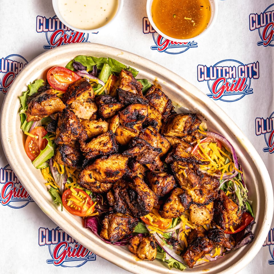 Grilled chicken salad with lettuce, tomatoes, onions, and cheese, with two dressings on the side.