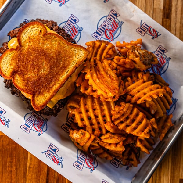 A Clutch City Grill burger with melted cheese on toasted bread, served with waffle fries.